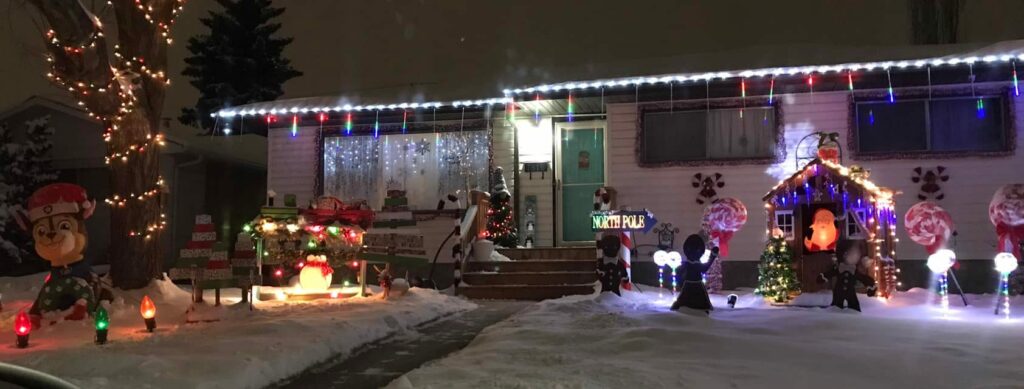 Night time front yard decorations with lit trees, inflatable Rudolf, penguins and snowman. Lollypops and a North Pole sign.